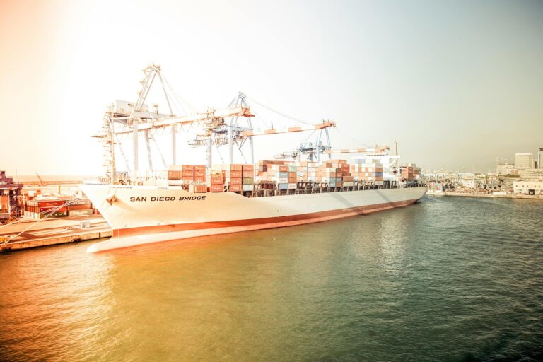 Container ship "San Diego Bridge" docked at a bustling harbor during sunset.