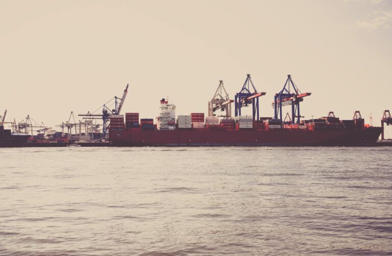 A cargo ship loaded with containers docked at a seaport under clear skies.