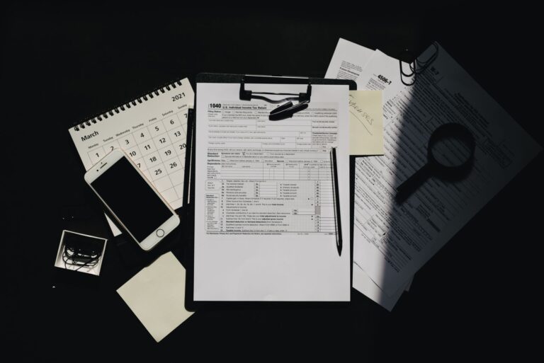 Flat lay of tax documents, calendar, and smartphone on a dark surface, symbolizing tax preparation.