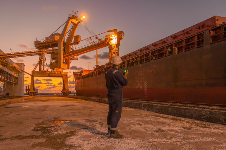 A dock worker examines a cargo ship under twilight skies at a Libyan port, highlighting industrial operations.