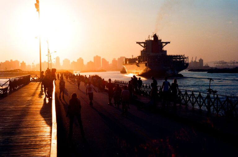 Silhouetted people and ship in Brazilian harbor during sunset, creating a vibrant skyline view.