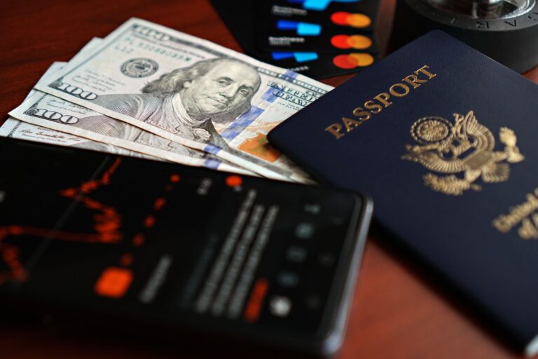 A flat lay of travel essentials including a passport, US currency, and credit cards on a table.