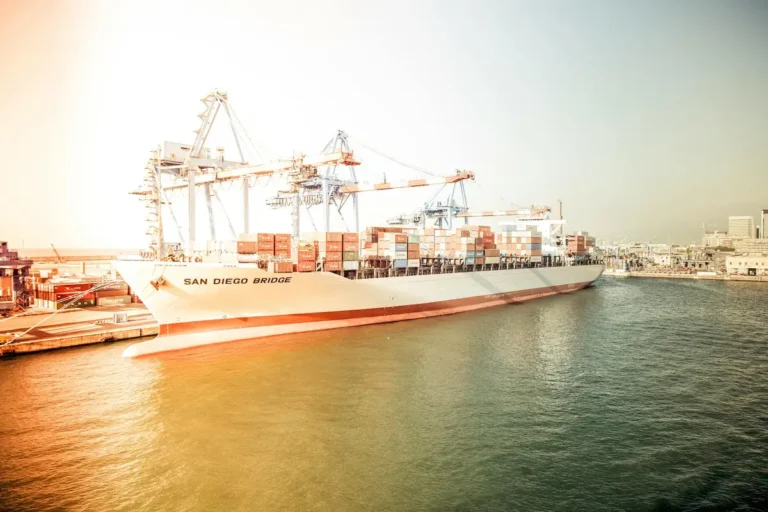 Container ship "San Diego Bridge" docked at a bustling harbor during sunset.