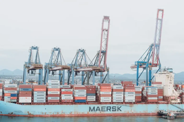 Container ship Maersk loading at a busy industrial port under cranes.
