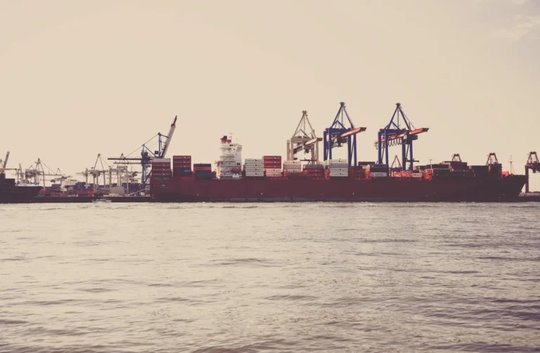 A cargo ship loaded with containers docked at a seaport under clear skies.